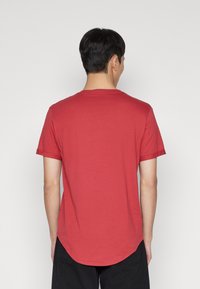 Camiseta de algodón roja con cuello redondo y mangas cortas, con un dobladillo curvado en la parte posterior para un ajuste relajado.