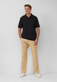 Schwarzes Polohemd mit kurzen Ärmeln, beigen Chinos und weißen Sneakers. Das Polohemd hat einen klassischen Kragen, eine lässige Passform und eine einfarbige Gestaltung.