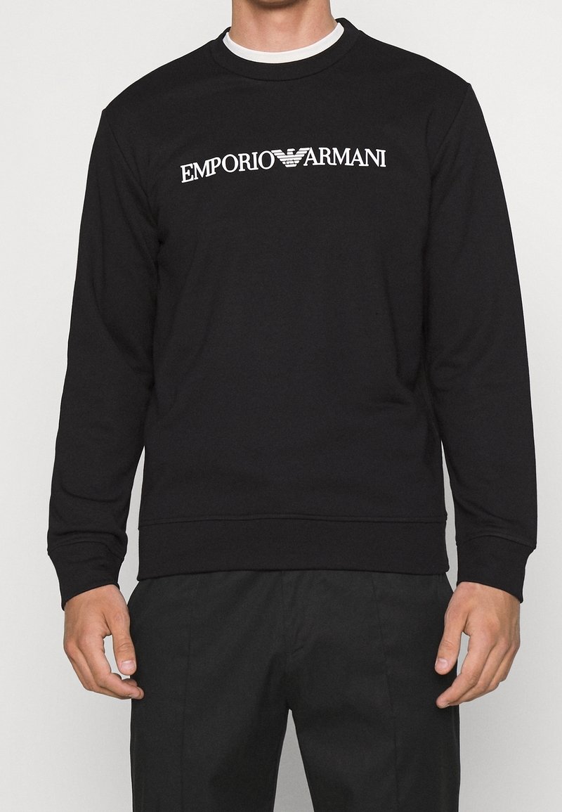 Felpa nera in cotone, con maniche lunghe e collo a girocollo a costine. La scritta bianca centrata recita "EMPORIO ARMANI."