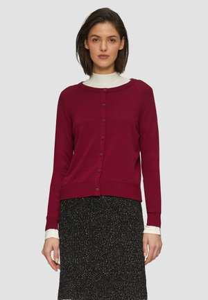Cardigan bordeaux avec un col rond, entièrement boutonné à l'avant, avec des poignets et un ourlet côtelés, porté sur une jupe noire à pois. Texture de tissu douce.