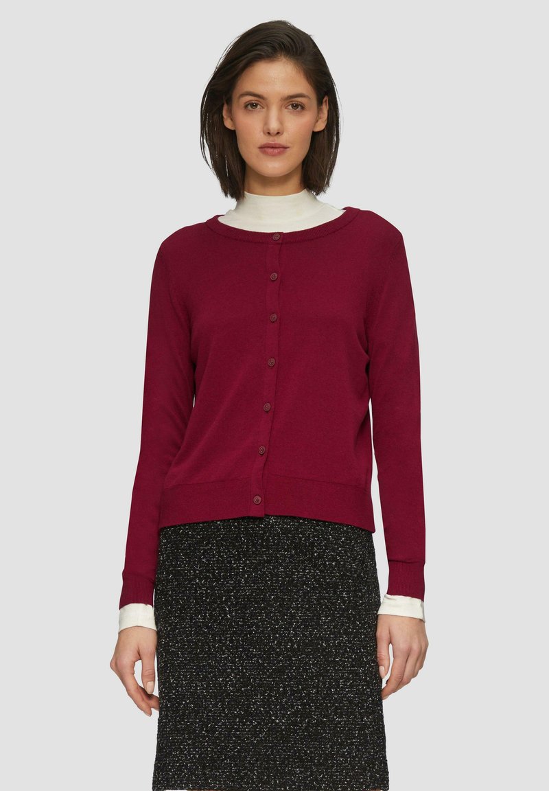 Bordeaux cardigan met een ronde halslijn, volledige knopenlijst, geribde manchetten en zoom, gedragen over een zwart gespikkelde rok. Zachte stoftextuur.