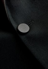 Sort stof med en tekstureret overflade, der har en rund sort knap og synlige syningsdetaljer på den foldede kant.