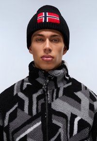 Berretto lavorato a maglia nero con design della bandiera della Norvegia. La giacca in pile presenta un motivo geometrico in nero, grigio e bianco. Chiusura frontale con zip.