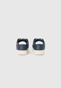 Navy blue leather sneakers with white accents, low-top design, textured heel, and a white rubber sole.