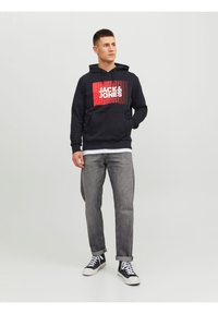 Felpa navy con un logo grafico rosso e bianco, tasca a marsupio e polsini a costine. Abbinata a jeans dritti grigio chiaro e sneakers nere.