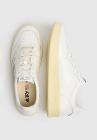 Sneakers bianchi in pelle con punta perforata, suola color crema e lacci tonali. Design minimalista con accenti di branding discreti.
