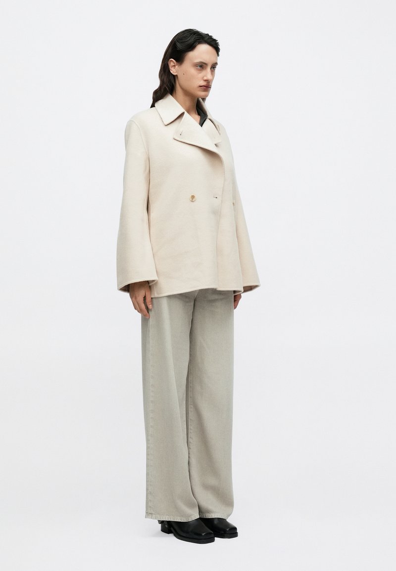 Beige double-breasted jacket with wide sleeves, paired with light gray wide-leg trousers and black ankle boots. Simple design with minimal details.