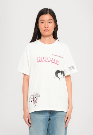 T-shirt en coton blanc avec le logo "KOOPLES" rose, des illustrations graphiques d'un couple et d'un chien, accompagnées de détails textuels sur le devant et sur le côté.