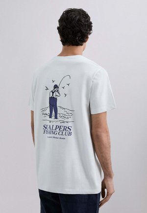 Hombre vistiendo una camiseta blanca con una ilustración de pesca y el texto "Club de Pesca Scalpers, canoas y barcos de motor" en la parte de atrás.