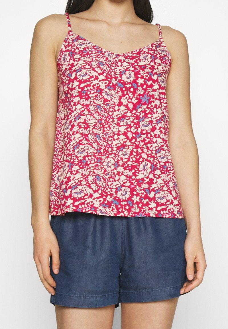 Camisola rosa a maniche corte con motivo floreale e scollatura a V, caratterizzata da fiori blu e bianchi. Abbinata a pantaloni corti in denim scuro.