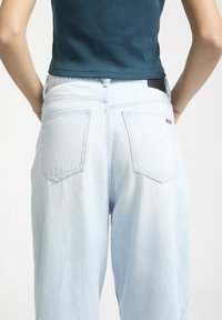 Lyseblå højtaljede jeans med en afslappet pasform, featuring to baglommer og et sort lædermærke i taljen.