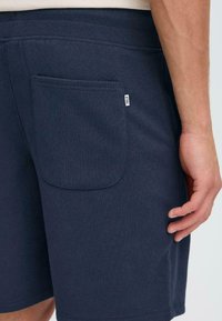 Shorts de sport bleu marine en tissu doux, avec une grande poche arrière avec étiquette, une taille élastique et des coutures lisses.