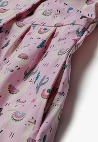 Tissu rose avec un imprimé ludique de lama et de cactus, avec des accents colorés, une texture lisse et un détail froncé le long de la couture.