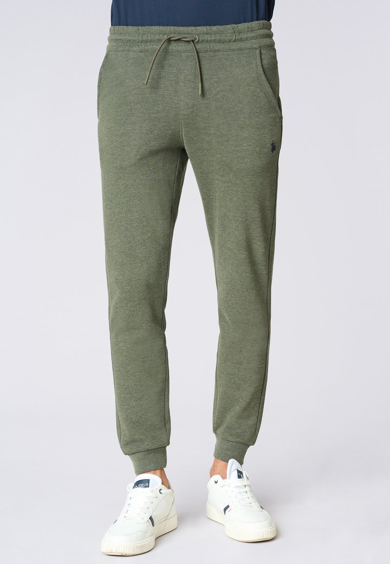 Pantaloni della tuta verde oliva con vita elastica e coulisse. Presentano tasche laterali e polsini a coste, realizzati in un tessuto morbido e strutturato.
