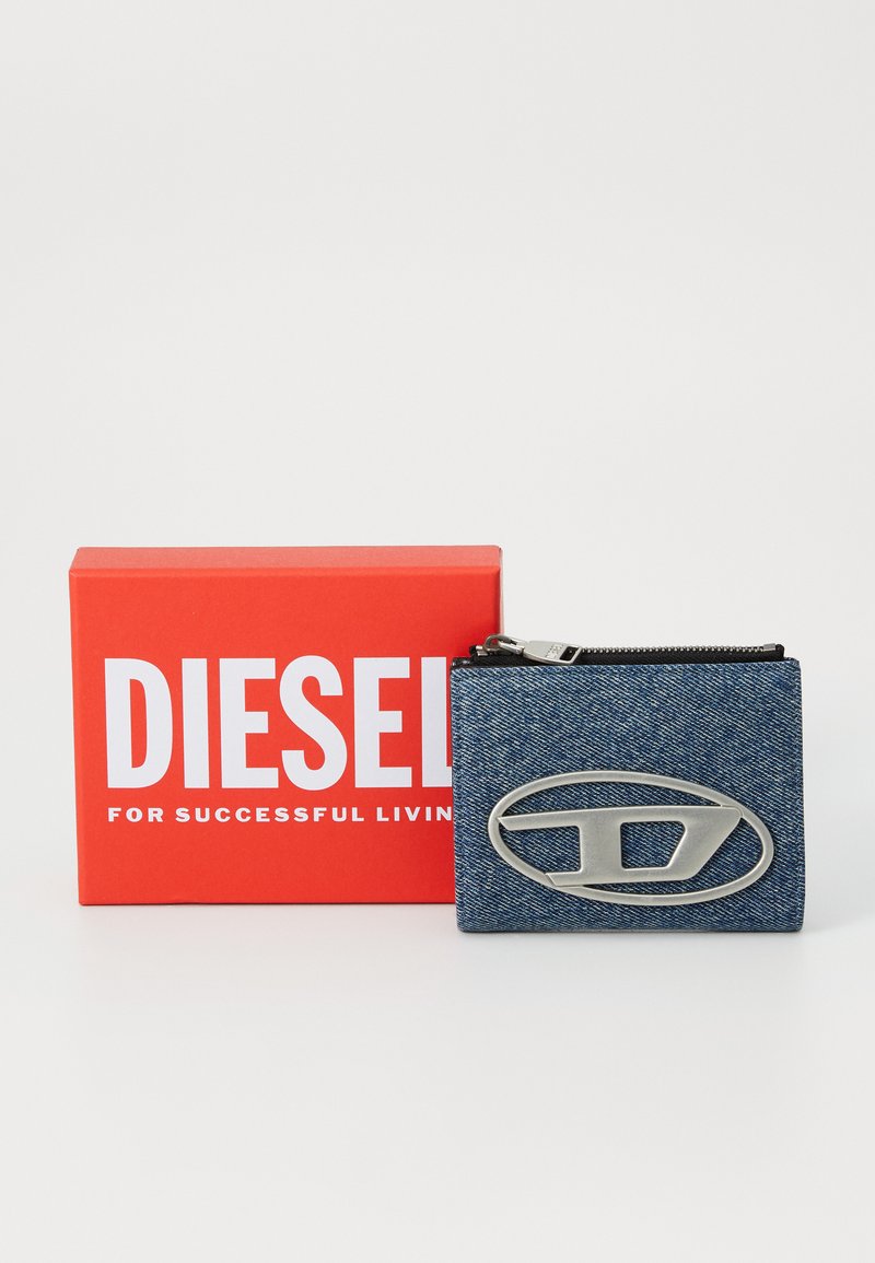 Portafoglio in denim con logo ovale argentato, dotato di chiusura a zip. Viene fornito con una scatola rossa con la scritta "DIESEL PER UNA VITA DI SUCCESSO."
