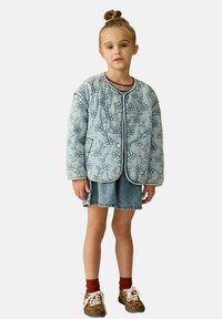 Gepatchte Denimjacke mit floraler Stickerei, blauen Tönen, rundem Kragen und Druckknöpfen, kombiniert mit einem Denim-Rock und gemusterten Schuhen.