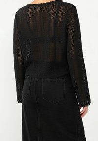 Czarny top dziergany na szydełku z długimi rękawami, o otwartej strukturze, okrągłym dekolcie i skróconym kroju, zestawiony z czarną spódnicą z wysokim stanem z denimu.