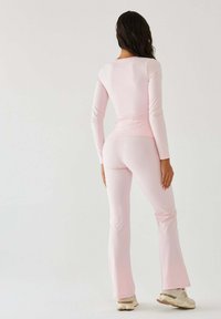 Różowa bluzka z długim rękawem w zestawieniu z różowymi, rozszerzanymi spodniami wykonanymi z lekkiej, elastycznej tkaniny. Charakteryzuje się gładką fakturą i dopasowanym krojem.