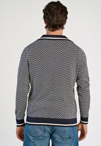 Maglione lavorato a maglia con un motivo a zigzag blu navy e bianco, polsini e orlo a coste, e colletto. La vista posteriore mostra il tessuto testurizzato e la vestibilità.