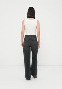 Svarte høytmidjede jeans med rak benklipp, med to baklommer, subtile sømdetaljer og en jevn tekstur. Parret med en hvit tank top.