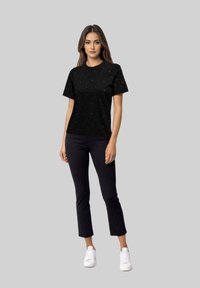 Camiseta negra de manga corta, con elementos decorativos dispersos, combinada con pantalones oscuros y zapatillas blancas. Ajuste y estilo casual.