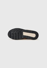 Semelle en caoutchouc noir avec un motif de grip texturé, accent de semelle intermédiaire beige et section de talon renforcé. Convient pour les activités de plein air.