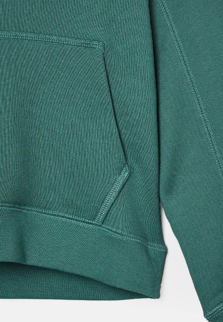 Tissu de sweat vert mettant en avant une poche kangourou, un ourlet côtelé et des coutures détaillées sur les manches et les bords de poche.