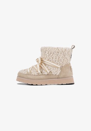 Beige suede boot with textured cream faux shearling upper, featuring decorative straps and a flat rubber sole. Loop pull tab at the back.