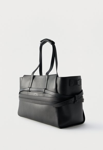 Μαύρη τσάντα ώμου από δέρμα με διπλές λαβές, πλαϊνά λουριά και δομημένο, ορθογώνιο σχήμα σε απλό ανοιχτό φόντο.