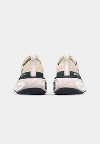 Nike Laufschuhe mit einem hellbeigen Obermaterial, dunklen grünen Akzenten, pinker Zwischensohle und schwarzem strukturiertem Außensohle. Mit Fersenlasche und Logo-Details.