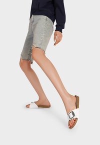 Sandali morbidi bianchi con una fascia ampia, fibbia argentata e soletta in sughero. Indossati con pantaloni corti di denim chiaro con orlo strappato.