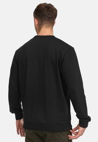 Sudadera negra de mangas largas, con cuello redondo y puños acanalados. La tela parece suave con una textura lisa y un detalle minimalista.