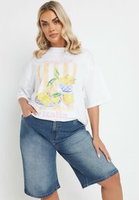 Valkoinen t-paita, jossa on värikäs sitruunagrafiikka kulhojen kanssa, yhdistettynä sinisiin farkkushortseihin. Väljä malli, jossa on lyhyet hihat ja rento muotoilu.