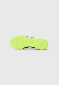 Semelle de chaussure de football, avec un caoutchouc néon jaune vif et des motifs de grip texturés, et une partie supérieure en thermoplastique noir.