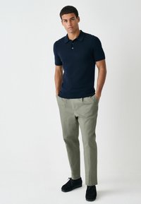 Tumesinine lühikeste varrukatega polosärk esikatte ja mustade kaunistustega, kombineeritud heleroheliste pükste ja mustade seemisnahast kingadega.