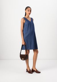 Vestido de ganga sem mangas com decote em V e design até ao joelho. Combinado com uma mala castanha e mocassins castanhos com um detalhe metálico.