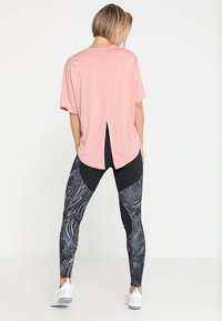 Camisa rosa de manga corta con una abertura en la espalda, combinada con leggings negros con un patrón abstracto en blanco y azul, y zapatillas deportivas blancas.