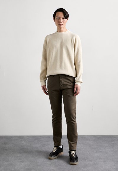 Strikket beige sweater, olivengrønne bukser og sorte sneakers med beige såler. Simpelt design, ribbet tekstur og kontrasterende snørebånd.
