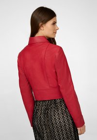 Veste en cuir rouge au design ajusté et col cranté, avec des détails de couture. Portée sur une jupe en dentelle noire.