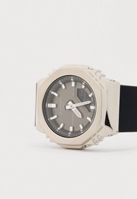 Ρολόι G-Shock με οκταγωνική θήκη σε ασημί απόχρωση, γκρι καντράν, λευκούς δείκτες ώρας και μαύρο λουράκι από καουτσούκ. Ανθεκτικό στο νερό έως 20 bar.