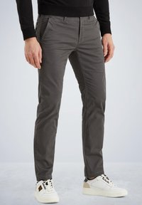 Graue Baumwollchinohosen mit slim Fit, Fronttaschen und Knopfverschluss; kombiniert mit weißen und beigen Sneakern mit schwarzen Schnürsenkeln.
