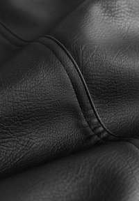 Tissu en cuir noir avec une surface texturée et des détails de couture visibles. Le matériau présente une apparence douce et souple avec un léger éclat.