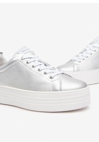 Baskets métalliques argentées avec une texture lisse, lacets blancs et une semelle plateforme blanche épaisse. Présente un logo sur la languette.