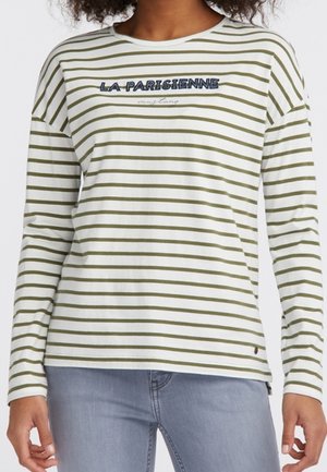 Mujer con camisa blanca de manga larga con rayas horizontales verde oliva y texto "LA PARISIENNE" en azul en el pecho, combinada con jeans azul claro.