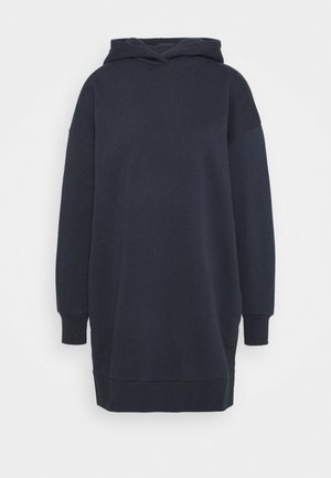 Długa ciemnogranatowa sukienka bluza z kapturem, długimi rękawami oraz prążkowanymi mankietami i dołem na jednolitym białym tle.