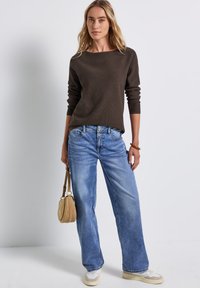 Maglione a maglia marrone, jeans blu a gamba larga, borsa beige, sneakers nel tono del beige. Design semplice, texture morbida, vestibilità casual. Nessun motivo o accento visibile.