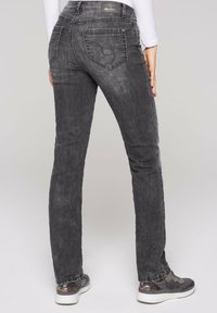 Vaqueros de mezclilla gris con un corte ajustado, cinco bolsillos y costuras sutiles en el bolsillo trasero, combinados con zapatillas con acentos metálicos.