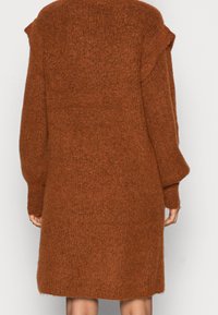 Robe-pull tricotée de couleur rouille avec manches longues et coupe décontractée. La texture semble douce et duveteuse, avec des épaules tombantes.