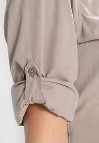 Manica di camicia color beige chiaro con risvolto, caratterizzata da un bottone di chiusura e una trama in tessuto leggera e liscia.