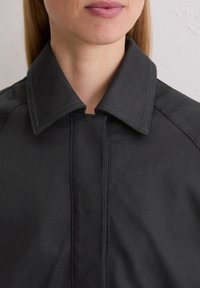 Czarna kurtka z tkaniny z ostrym kołnierzem, z widocznymi detalami szwów i gładką teksturą. Zbliżenie na obszar dekoltu.